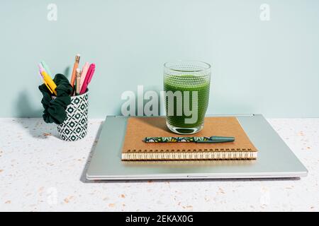 Gesunder grüner Saft, Buch, Stift und Laptop über Schreibtisch gegen Wand zu Hause Stockfoto