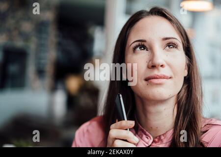 Nachdenkliche weibliche Profikanin mit Handy, das im Café nachschaut Stockfoto