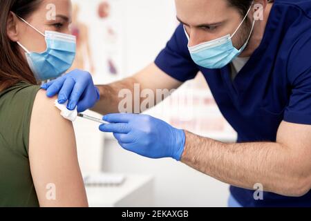 Männlicher Arzt, der während einer Pandemie einer Patientin in der Klinik eine Impfung verabgab Stockfoto