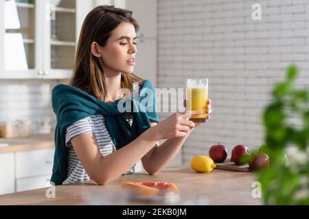 Junge Frau hält ein Glas Saft in der Nähe von frischem Obst Verschwommener Vordergrund Stockfoto