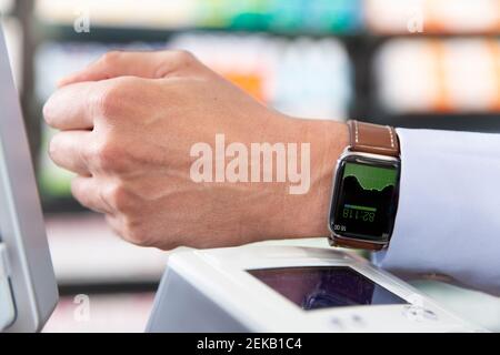 Männlicher Kunde, der kontaktloses Bezahlen durch Smart Watch in der Apotheke macht Stockfoto