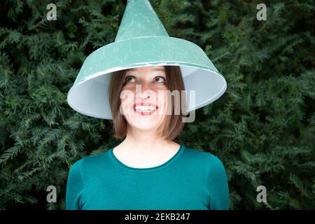 Glückliche Frau mit Lampenschirm auf Kopf gegen Pflanze Stockfoto