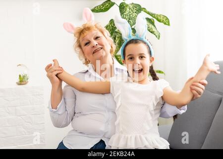 Frohe Ostern. Eine Großmutter und ihre Enkelin malen Ostereier. Glückliche Familie bereitet sich auf Ostern vor. Nettes kleines Kind Mädchen trägt Hasenohren Stockfoto