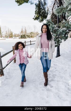 Lächelnde Mutter und Tochter halten sich die Hände, während sie im Park spazieren Stockfoto