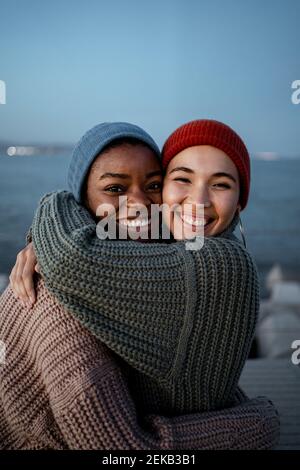 Glückliche junge Frauen umarmen sich gegenseitig, während sie gegen den Himmel stehen Stockfoto