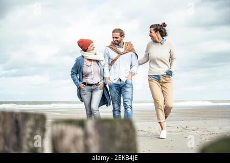Gruppe von Freunden, die gemeinsam entlang des sandigen Küstenstrandes spazieren Stockfoto