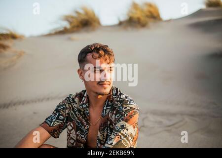 Schöner Mann, der auf Sand in Almeria, Wüste Tabernas, Spanien, sitzt Stockfoto
