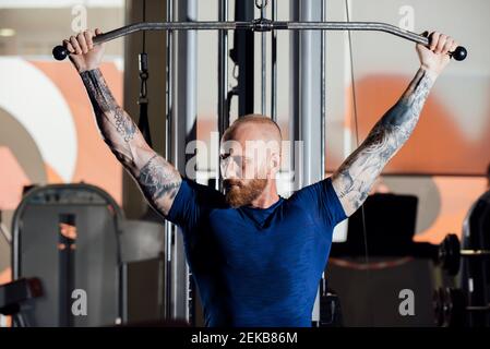 Sportler trainieren, während sie auf der Lat Pull-down-Maschine sitzen Fitnessraum Stockfoto