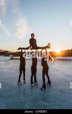 Weibliche Eiskunstläuferinnen üben auf gefrorenem See bei Sonnenuntergang Stockfoto