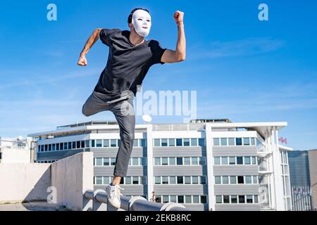 Junger Mann mit weißer Maske läuft auf dem Dach während der Sonne Tag Stockfoto