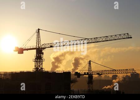 Silhouetten von Baukräne und unfertigen Wohngebäuden auf Sonne und Rauch Hintergrund. Wohnungsbau, Wohnblock Stockfoto