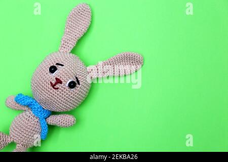 Osterhase auf grünem Hintergrund. Grußkarte mit gestricktem Spielzeug Kaninchen mit freiem Kopieplatz Stockfoto