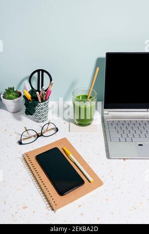 Laptop, gesunder grüner Saft, Buch, Handy und saftige Pflanze über dem Schreibtisch zu Hause Stockfoto