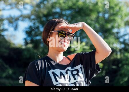 Nahaufnahme einer schönen Frau, die eine Sonnenbrille trägt und die Augen vor Bäumen schützt Im Park Stockfoto