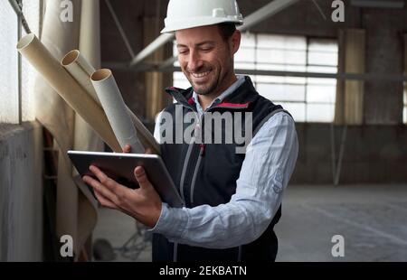 Lächelnder Bauunternehmer mit digitalem Tablet, während er auf der Baustelle steht Standort Stockfoto