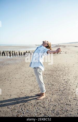 Junger Mann mit ausgestreckten Händen, der bei Sonnenschein am Strand steht Tag Stockfoto