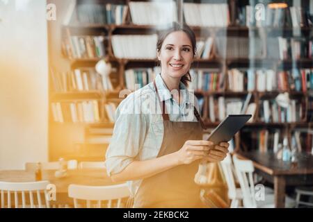 Lächelnde Managerin, die wegschaut, während sie das digitale Tablet in der Hand hält Café-Bar Stockfoto