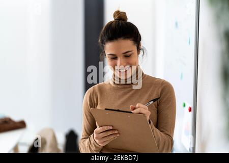 Glücklich junge Studentin Schreiben auf Zwischenablage während des Studiums in Wohnzimmer Stockfoto