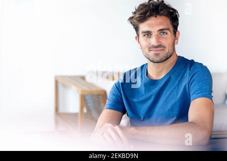 Schöner Mann mit blauen Augen lächelnd, während er zu Hause sitzt Stockfoto