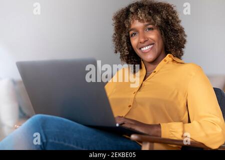 Frau mit mittlerem Erwachsenen und Laptop, der beim Sitzen wegschaut Zu Hause Stockfoto