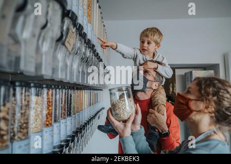 Vater und Sohn einkaufen im Einzelhandel, während sie stehen Weibliche Besitzerin während einer Pandemie Stockfoto