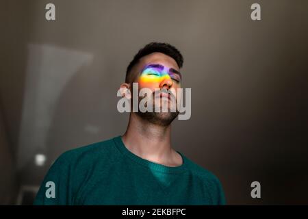 Regenbogen Licht trifft Gesicht des jungen Mannes im Innenbereich mit Geschlossene Augen Stockfoto