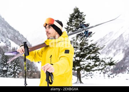 Nachdenklicher Mann mit Ski, der auf Schnee steht und wegschaut Bedecktes Tal Stockfoto