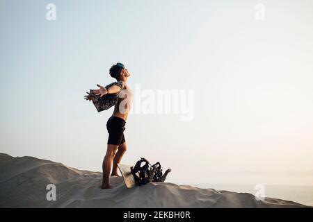 Junger Mann mit ausgestreckten Armen steht am Sandbrett in Wüstenshorts in Almeria, Tabernas, Spanien Stockfoto