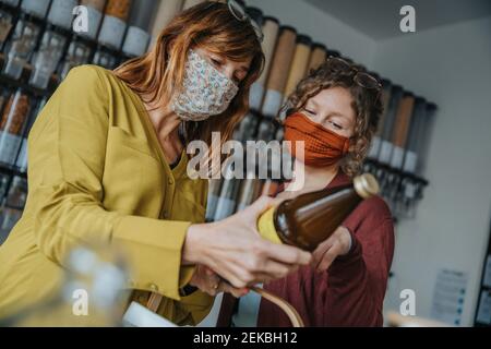 Weibliche Freunde überprüfen Etikett auf Trinkflasche, während sie im Stehen Zero Waste Store während COVID-19 Stockfoto