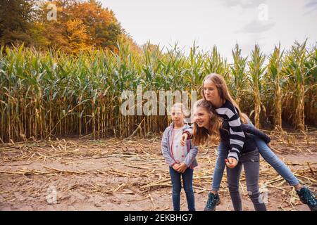 Lächelndes Mädchen Huckepack Freunde beim Stehen auf Maisfeld Stockfoto