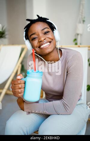 Lächelnde Frau mit Einmachglas sitzt auf dem Liegestuhl Wohnzimmer Stockfoto