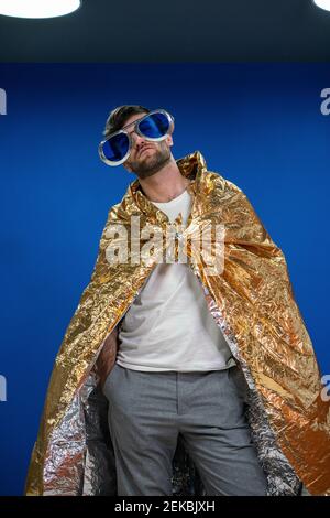 Männliche Unternehmer in Neuheit Gläser tragen Gold Farbe Geschenkpapier cape gegen blaue Wand am Arbeitsplatz Stockfoto