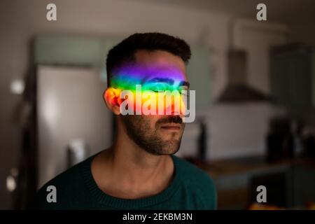 Regenbogen Licht trifft Gesicht des jungen Mannes im Innenbereich mit Geschlossene Augen Stockfoto