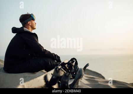 Junger Mann mit Schutzbrille sitzt am Sandbrett in der Wüste in Almeria, Tabernas, Spanien Stockfoto