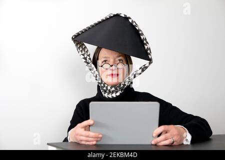 Frau trägt schwarzen Lampenschirm hält digitale Tablette gegen weiß Wand Stockfoto