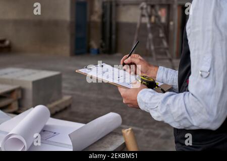 Nahaufnahme eines männlichen Architekten, der im Stehen auf einem Dokument schreibt Gebäude Stockfoto