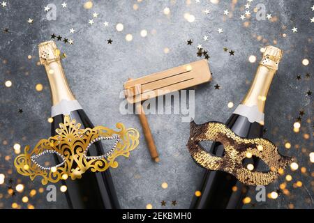 Zwei Champagnerflaschen, goldene Karnevalsmasken. Noisemaker- und Konfetti-Sterne auf grauem Hintergrund. Purim Karnevalsfeier Konzept Stockfoto