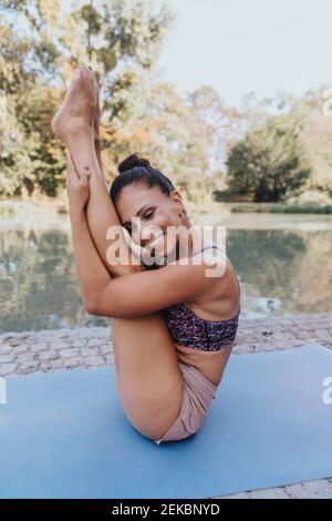 Lächelnde Sportlerin, die mit den Füßen nach oben sitzt, während sie Yoga praktiziert parken Stockfoto