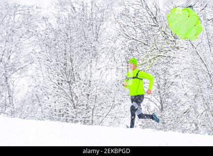 Männlicher Athlet mit Fallschirm läuft auf Schnee im Wald während Winter Stockfoto