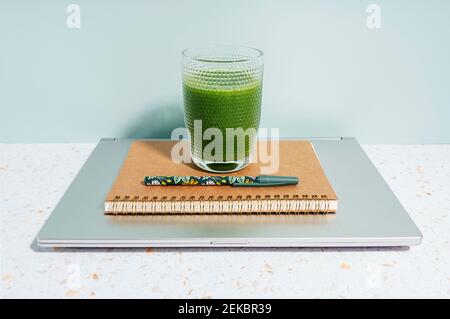 Gesunder grüner Saft, Buch, Stift und Laptop über dem Schreibtisch an der Wand Stockfoto