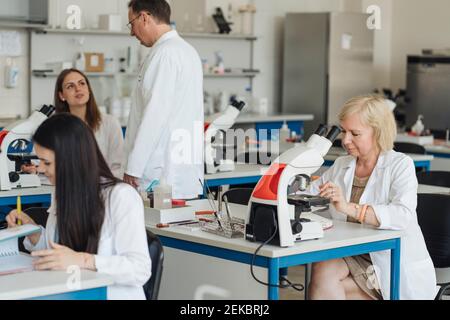 Leitende Forscherin in einem weißen Mantel, die im Labor arbeitet Umgeben von anderen Forschern Stockfoto