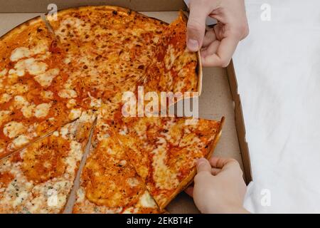 Zwei Hände nehmen Scheiben Pizza aus Karton Stockfoto