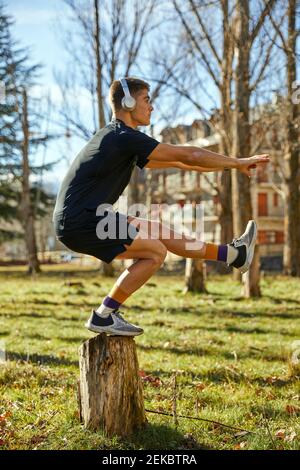 Entschlossener männlicher Athlet balanciert auf Baumstumpf im Park auf Sonniger Tag Stockfoto