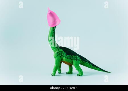 Diplodocus Dinosaurier Spielzeug mit rosa Menstruationstasse auf dem Kopf Auf mintgrünem Hintergrund Stockfoto