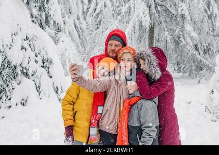 Reife Frau, die Selfie mit der Familie nimmt, während sie im Wald steht Während des Schnees Stockfoto