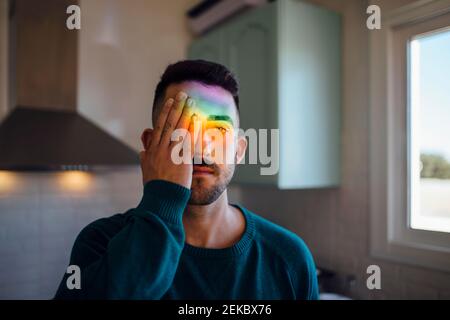 Regenbogenlicht trifft Gesicht des jungen Mannes, der ein Auge bedeckt Mit der Hand Stockfoto