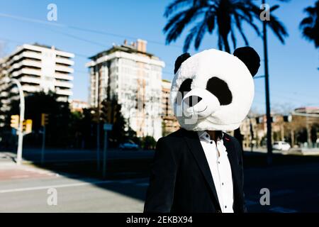 Geschäftsmann mit Panda-Maske, der in der Stadt steht und wegschaut Stockfoto
