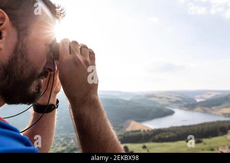 Junger Mann beim Blick durch Fernglas im Sonnenlicht während Urlaub Stockfoto