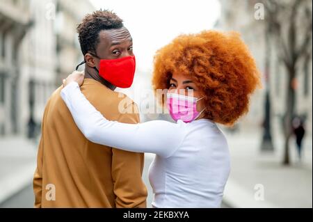 Frau trägt Gesichtsmaske mit Arm um auf Mann stehen Im Freien Stockfoto