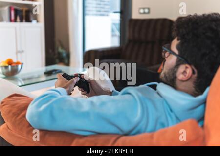 Entspannter junger Mann, der Videospiel spielt, während er auf dem Sofa sitzt Im Wohnzimmer Stockfoto